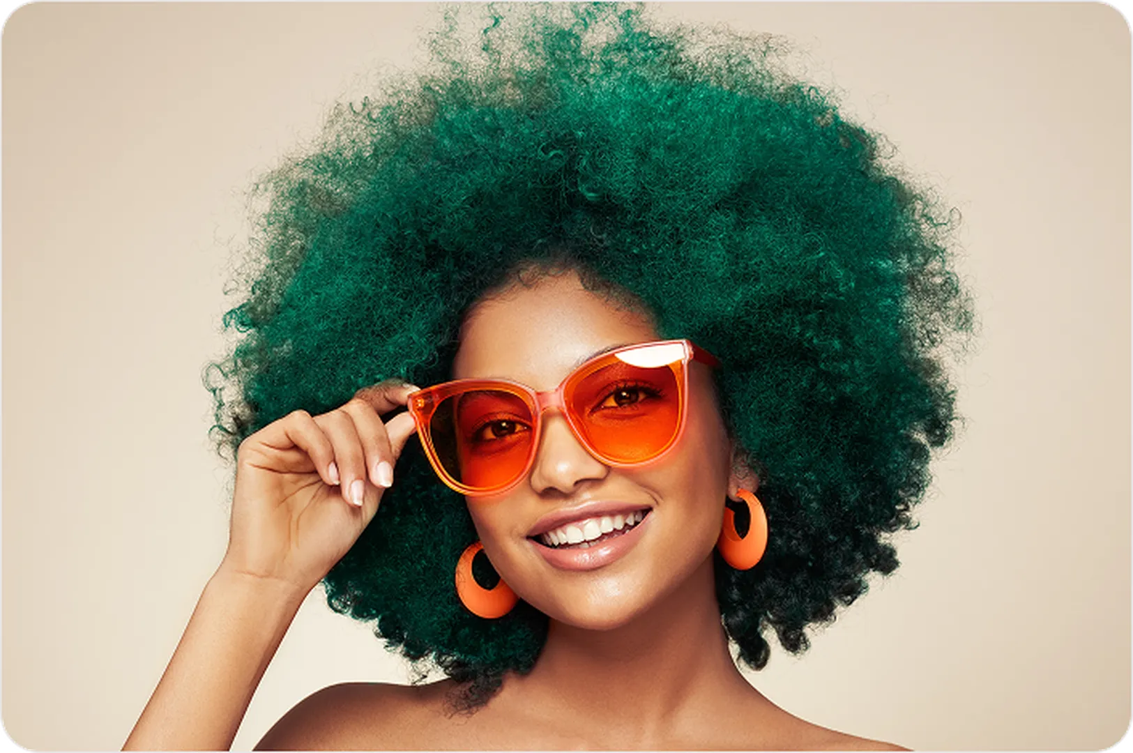 Green curly-haired person with orange sunglasses & earrings on light beige background.