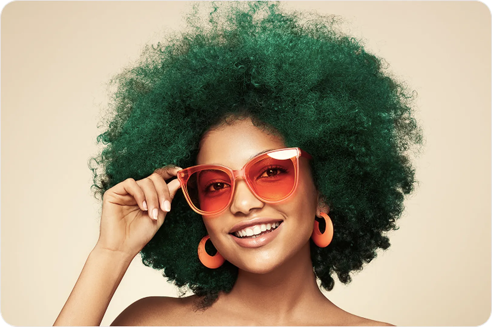 Green curly-haired individual wearing orange sunglasses and earrings against a light-beige backdrop