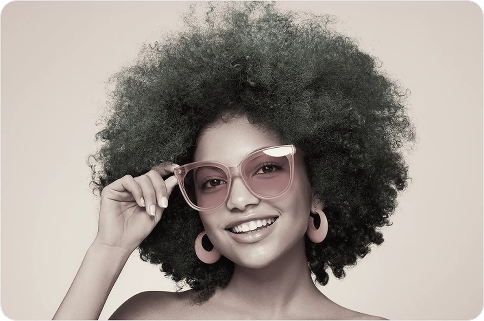 Curly-haired person with pink sunglasses & earrings on soft beige background.