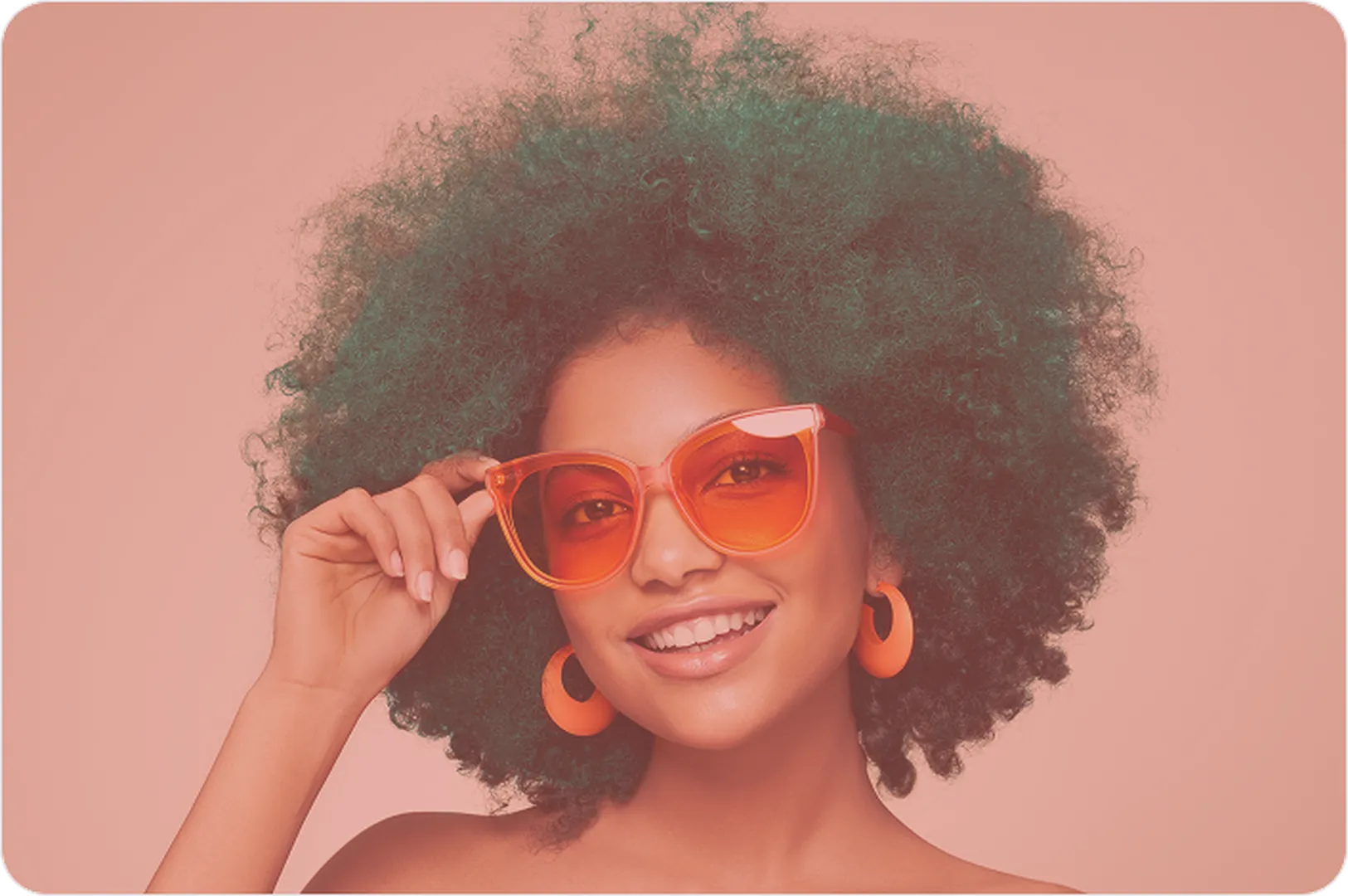 A woman with an afro and sunglasses stands against a vibrant pink background.